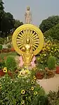 Seated statue of the Buddha, with standing Buddha statue in the background, on the grounds of the Thai temple and monastery at Sarnath