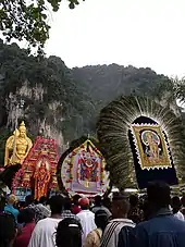 Icons carried in procession during Thaipusam at Batu Caves. Also seen in the background is the 42.7 m high golden statue of Murugan.