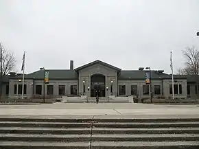 Photograph of the front of a classical-style, gray one-story building, with large front landing and steps