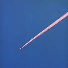 A pink contrail cloud streaking across a clear blue sky.