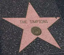 A pink star engraved into a black tile. The words in the center of the star read "THE SIMPSONS", and below them is a pictogram of a television.