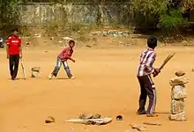 Three Hyderabadi boys playing with cricket bats and a ball