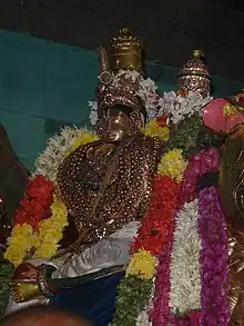 The metal idol of a man decorated with jewellery and flower garlands on whose thigh a woman is seated.