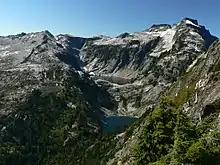 Looking down into a valley below a high mountain on the right and a slightly smaller one on the right. In between are two lakes, one noticeably higher than the other. The lower reaches of the mountain and the area of the lakes have plant growth.