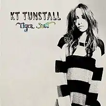 A greyscale photo of Tunstall wearing a striped jumper, standing against a white background. On the left of the image the words "Tiger Suit" and the name "KT Tunstall" are placed in a stylised font.