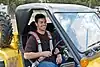 A man in his early thirties is smiling and sitting inside a yellow tomcar and strapped inside by a seatbelt