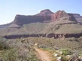 View of Tower of Set peak and sub-unit cliff section from Tonto Trail, Granite Gorge, north of Mohave Point, Grand Canyon Village, South Rim. The peak is behind and separated from a cliff unit (with small prominence), in front-(photo center, right, Tower of Set (peak) to its left). Vertical erosion in cliff of Redwall Limestone, upon horizontal Muav Limestone cliff. The Tapeats Sandstone sits in foreground on Granite Gorge,  and is seen as thinly-bedded. The slope-former above is the (dull-greenish)-Bright Angel Shale with thin, inter-bedding, as well as one resistant cliff unit. The Redwall Limestone cliff section in Grand Canyon is about 450 feet (137 m) thick.