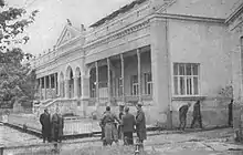 Large, light-coloured building with warmly-dressed people outside