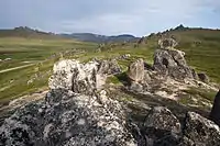 View from the top a hill of a grassy valley and rocks in the foreground