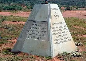 Pyramid-shaped stone marker. One side reads: "Test site Totem 1. A British atomic weapons was test exploded here on 15 Oct 1953." The other side reads: "Warning: radiation hazard. Radiation levels a few hundred metres around this point may be above those considered safe for permanent occupation."