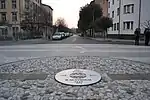 Metal plaque installed in 2004 in the middle of the square at the border point, once crossed by the "Gorizia Wall [it]" [the latter separated Slovenian Yugoslavia from Italy, and during this era border controls were carried out the same way as along Berlin wall, moreover this was strengthened with barbed wire to prevent escapes [citation needed]]