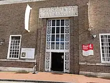 Entrance of large brick building with decorated windows and stone relief carving above doorway