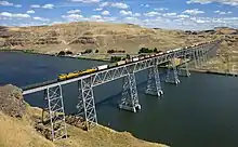 A freight train crosses a wide river on a steel bridge