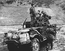 Several soldiers working around a machine gun mounted on a half-track