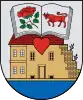 A coat of arms depicting an open book with a red rose on one page and a red bull on the other all hovering over a red heart with a building in the background