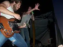 Two men performing onstage, one playing a guitar and the other singing into a microphone