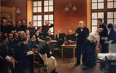 A painting of a group of men in a classroom, with one man lecturing. At right, a hypnotized woman is helped up by another man and a female nurse.