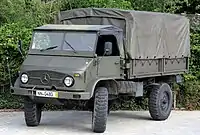 A military Unimog S 404 truck painted in camouflage in front of a forest background.