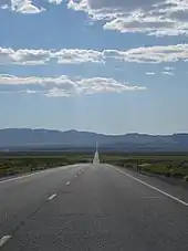 View across a desert valley with a highway proceeding straight for many miles towards the horizon and a distant mountain range