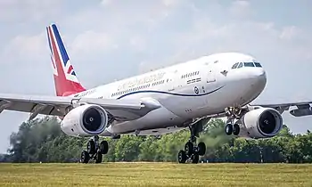 A gloss white painted Airbus A330 with a red, white and blue 'Union Jack' flag on its vertical tail fin and UNITED KINGDOM in gold lettering on its upper fuselage, operated by the Royal Air Force, which has been modified for military and VIP use, is about to land RAF Brize Norton in Oxfordshire, England.