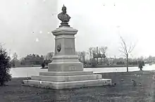 A bust of Kaiser Wilhelm I of Germany stands atop a pedestal along the shore of a small lake.