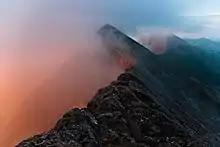 a series of jagged mountain peaks with a pinkish fog rising on the left side