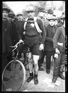 A man posing with a bike while wearing a hat.