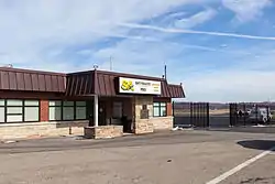 Single-storey building with a sign reading "SA Skyward Aviation FBO Washington County Airport" with a propeller plane and a fuel tanker in the background