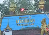 Traffic lights, a blue sign with golden letters saying "Welcome to MYANMAR THE GOLDEN LAND".