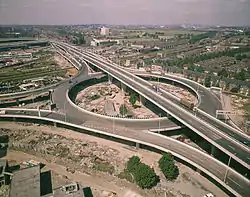 Aerial view of elevated roundabout with flyover passing above and slipways joining from three directions. Construction appears to have recently finished.