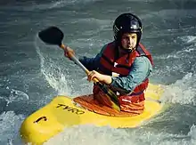 Photo of man in kayak holding paddle nearly parallel to the boat, surrounded by white water