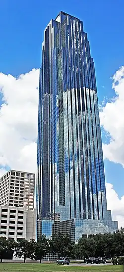 Tall, symmetrical, glass skyscraper with triangular peak, and setbacks that narrow the building as it rises. A chevron design under the top seems to be pushed upward by a long, thin arrow.