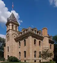 A plain three-story, stone building with a clock tower on the left side.