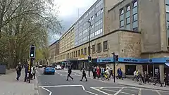 A busy street with tall trees on one side and stark modern buildings on the other