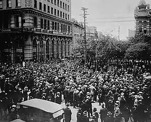 Large group of people in the middle of a city street beside a large concrete building