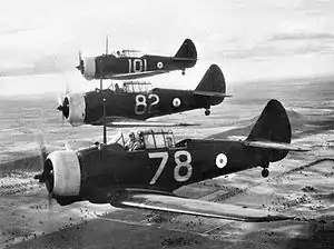 Three World War II-era single propeller aircraft flying in formation over a town