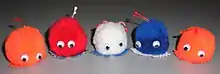 Five fluffy Weepul toys with a pair of googly eyes each; orange, red, white, blue, and orange in order, all with white and black googly eyes