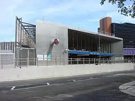 A silver metal and glass building with a blue sign with "WOOD LANE STATION" in white letters