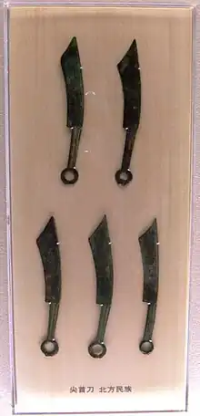 Five elongated bronze knives, corroded over time with a green color, with a ring handle on the end opposite the blade